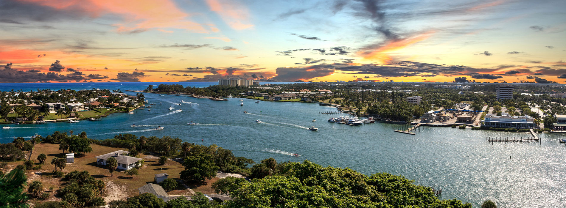 The image shows a scenic view of a harbor at sunset with boats on the water, a city skyline in the background, and a colorful sky above.