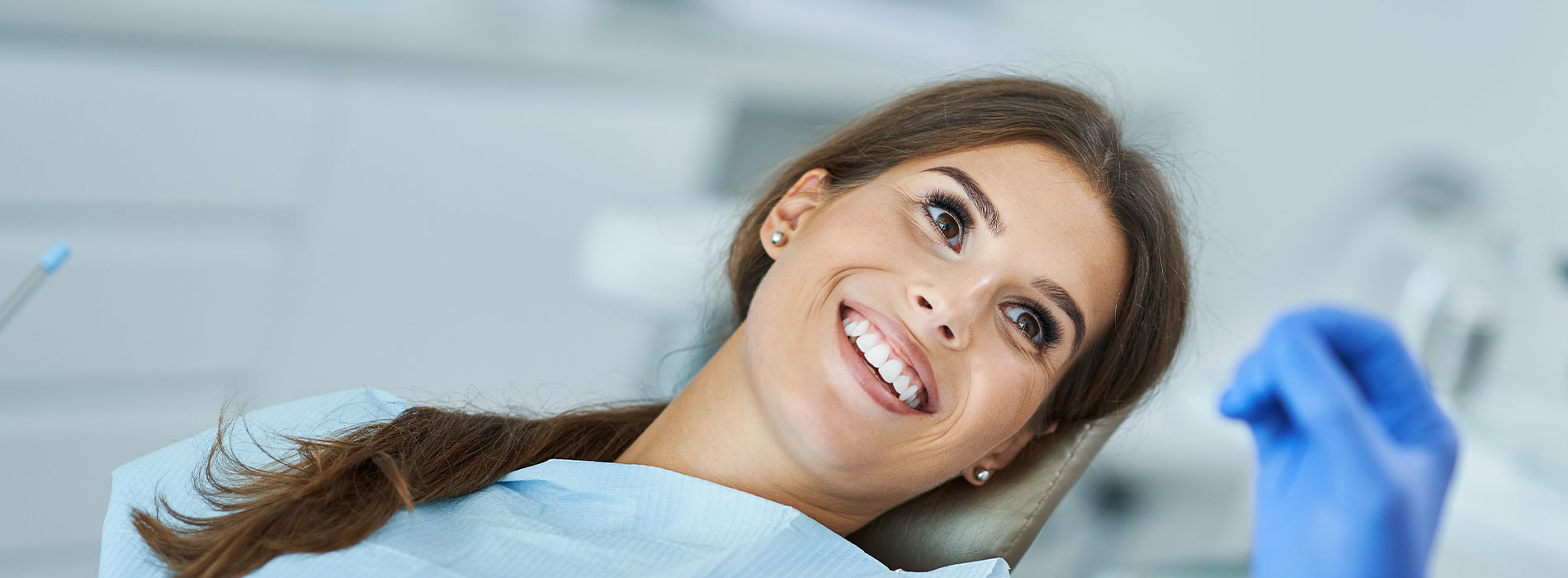 The image is a photograph of a woman with light skin, smiling at the camera. She appears to be in her late twenties or early thirties and has long hair. Her eyes are looking directly at the camera, and she is holding up her index finger near her mouth as if she s making a point or emphasizing something. The background is plain and light-colored, which suggests that this could be a stock photo used for various purposes such as advertising, personal branding, or lifestyle content.
