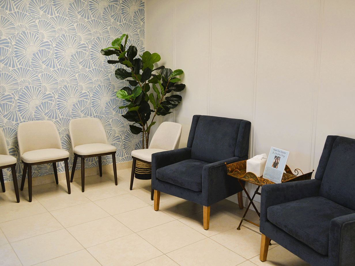 An interior room with blue wallpaper featuring a floral pattern, several chairs, a potted plant, and a waiting area setting.
