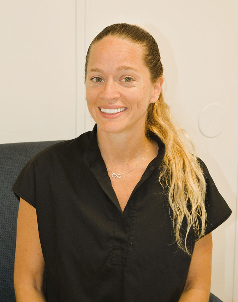 A woman with blonde hair and a ponytail wearing a dark top poses for a portrait photo.