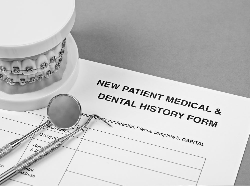 Alt text A photograph of a document with the title NEW PATIENT MEDICAL HISTORY DENTAL HISTORY prominently displayed, accompanied by a pair of scissors and a small dental model.