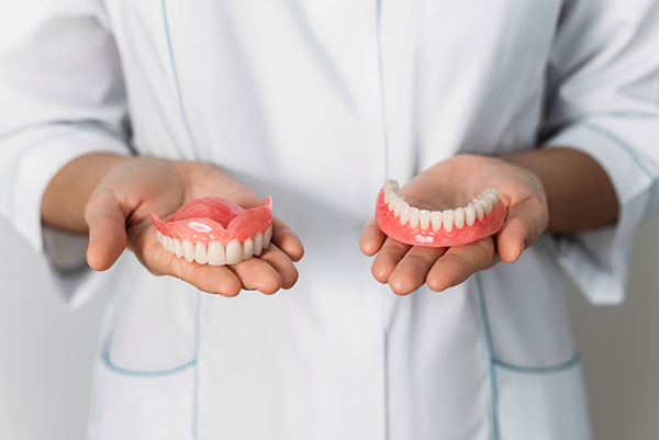 person holding two dentures, one upper arch and one lower arch